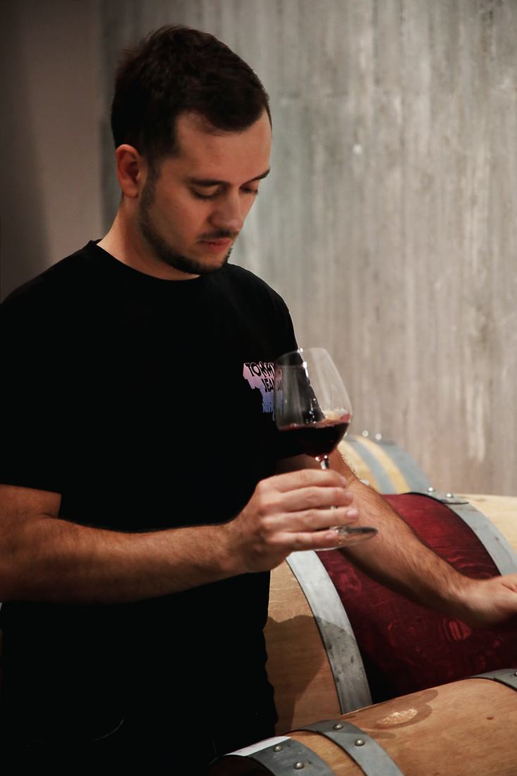 Ludovico Berta con un calice di rosso accanto alle botti
